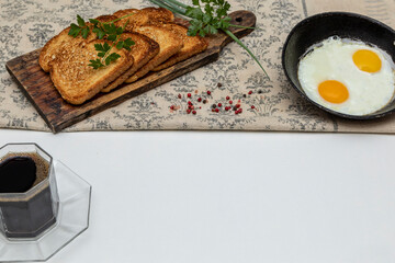 Fried eggs in a rustic iron pan, toast on a wooden board and a cup of coffee for breakfast.