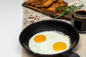 Fried eggs in a rustic iron pan, toast on a wooden board and a cup of coffee for breakfast.