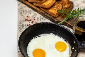Fried eggs in a rustic iron pan, toast on a wooden board and a cup of coffee for breakfast.