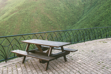 Wooden picnic table with benches on a paved terrace overlooking green forested mountains, peaceful...