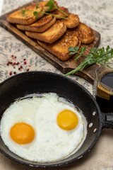 Fried eggs in a rustic iron pan, toast on a wooden board and a cup of coffee for breakfast.