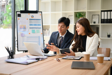 Businessman and businesswoman working together at a modern office desk, discussing data on a laptop
