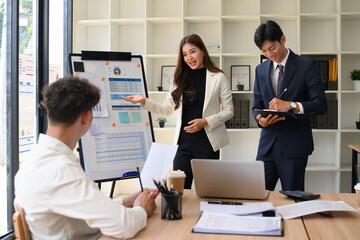 Confident businesswoman presenting charts on a whiteboard to colleagues in a modern office. Teamwork and strategy planning with data visuals