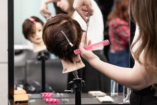 Close-up of student hands using scissors to cut synthetic hair on mannequin in beauty training session
