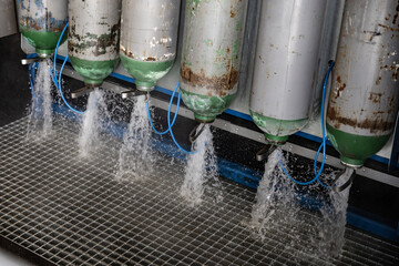 Rusted green and silver gas cylinders expelling water in a testing or maintenance station with...