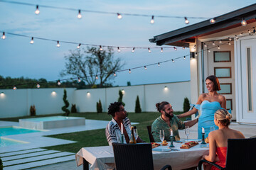 Friends enjoying dinner party in backyard with swimming pool