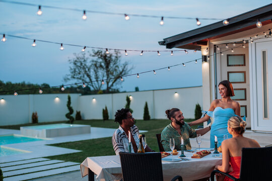 Friends enjoying dinner party in backyard with swimming pool