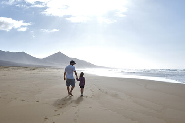 father and daughter walking along the sandy beach holding hands