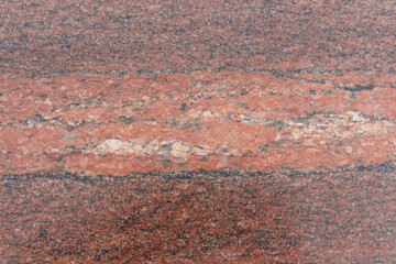 Close-up view of a rugged reddish granite stone surface showcasing unique natural patterns and textures. This stone features a diverse array of mineral inclusions, creating visual interest.