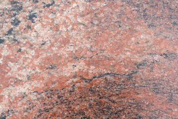Close-up view of a rugged reddish granite stone surface showcasing unique natural patterns and textures. This stone features a diverse array of mineral inclusions, creating visual interest.