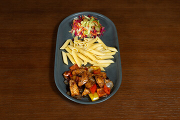 Chicken in sweet and sour sauce. Chicken wings in sweet and sour sauce on a plate with pasta and salad mix on a table in a restaurant