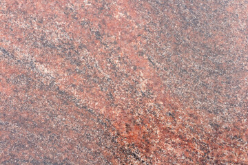 Close-up view of a rugged reddish granite stone surface showcasing unique natural patterns and textures. This stone features a diverse array of mineral inclusions, creating visual interest.