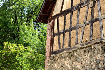 An old brown half-timbered barn, standing quietly with a lush green garden stretching out behind it.