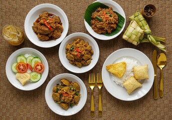 Overhead view of indonesian dishes and ketupat on a textured brown surface