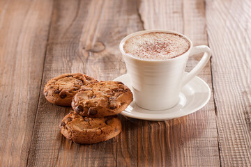 Oatmeal chocolate chip cookies with cup of coffee on wooden background.