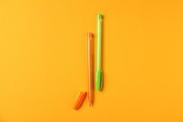 Stylish pens on orange background, flat lay