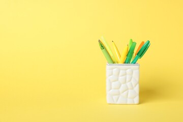 Ballpoint pens in holder on yellow background. Space for text