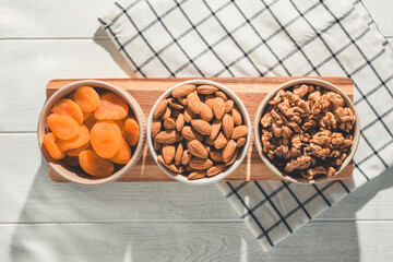 Three bowls of healthy snacks including dried apricots, walnuts, and almonds are arranged on a...