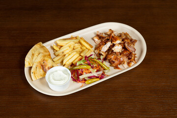 Doner on a plate with chicken French fries bread mixed salad and garlic sauce in a plate on the table
