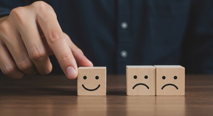 Hand choosing a happy face wooden block over sad face blocks on wooden table