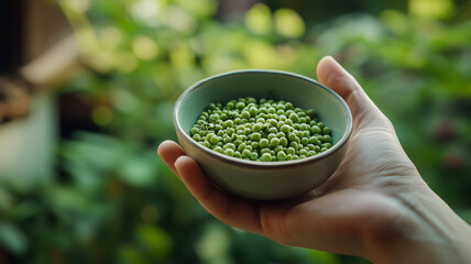 A hand holding a small bowl of freshly shelled peas with a lush green garden visible in the background