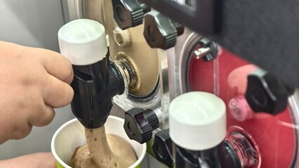 Person Filling Cup with Delicious Soft Serve Ice Cream from a Commercial Machine in a Busy Shop Environment