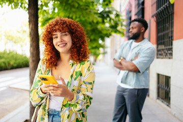 Fototapeta premium Young woman using smartphone while man waiting on the street