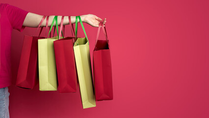 Caucasian adult holding shopping bags with multicolored handles against red background
