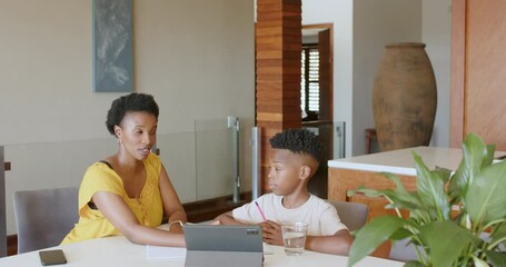Mother helping son with homework using tablet at home, both concentrating - Powered by Adobe