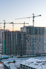 Construction site, cranes and multi-storey unfinished buildings at sunrise or sunset