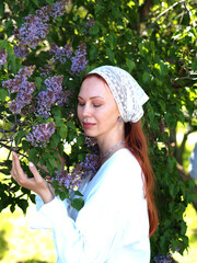 Portrait of a beautiful red-haired young woman in a headscarf in lilac blossom blossoms