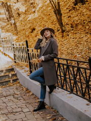 Beautiful blonde young woman in hat and coat walking on the stairs in the autumn park.
