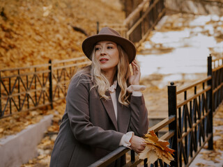 Beautiful blonde young woman in hat and coat walking on the stairs in the autumn park.