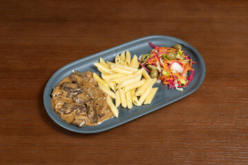 Beef in cream sauce. Beef in cream sauce on a plate with pasta and salad mix on a table in a restaurant