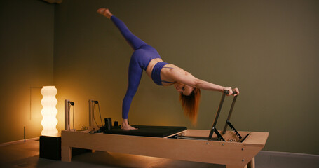 Woman doing pilates exercise on Pilates Reformer for the chest and back muscles, focusing on flexibility, strength, and control with determination