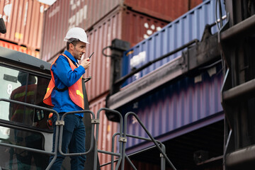 Caucasian man engineer worker working with walkie talkie and talking on Reach Stacker at container...