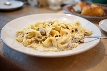 Creamy fettuccine pasta dish served on a white plate with fork resting beside it on a rustic table