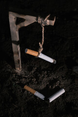 High-angle shot of a cigarette hanging from a rope above the ground, with another cigarette split in half at its base. It symbolizes the concept of quitting the smoking habit.