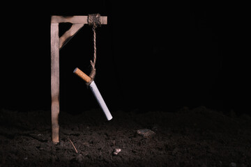 Cigarette hanging from a rope on a medieval gallows, with black background. Concept of quitting smoking. Copy space.