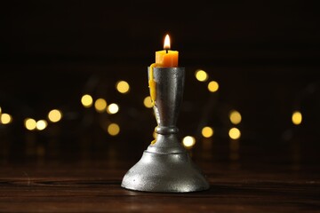 Burning candle in candlestick on wooden table against dark background with blurred lights. Bokeh...