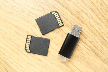 Flash drive and SD memory cards on wooden background, flat lay