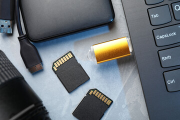 Flash drive connected to laptop, SD memory cards, external hard disk and camera lens on gray...