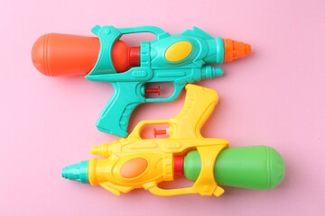 Bright plastic water guns on light pink background, top view