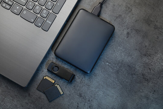 SD memory cards, USB flash drive, hard disk drive with cable and laptop on dark grey table, flat lay. Space for text