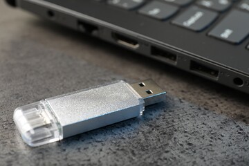 USB flash drive and laptop on dark grey table, closeup