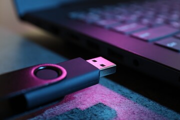 USB flash drive and laptop on dark grey table, closeup