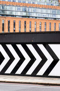 Black and white chevron pattern painted on urban barrier with modern building facade in background. Graphic contrast and directional visual element for editorial or design themes.