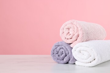 Clean towels on light marble table against pink background, space for text