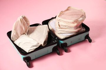 Open suitcase with packing cubes on pink background