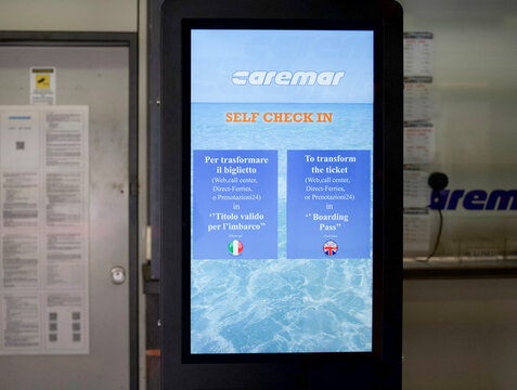 Naples, Italy - April 23, 2025: Caremar self check-in kiosk displaying ticket transformation instructions in Italian and English, with blue ocean background, enhancing user experience 